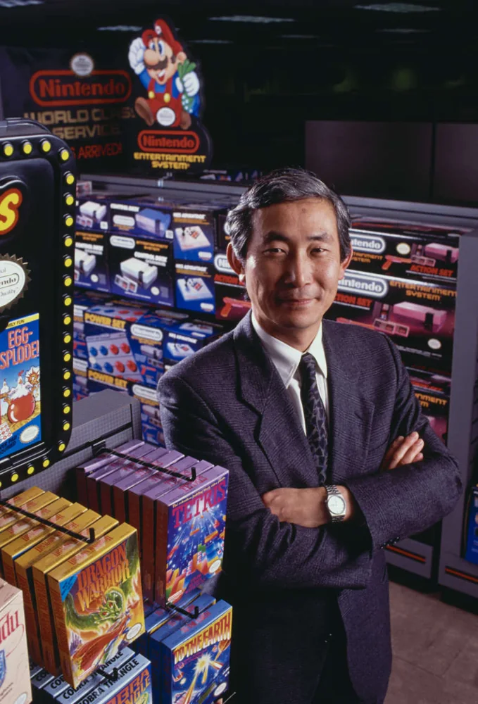 Minoru Arakawa standing beside Nintendo game boxes and a retail display