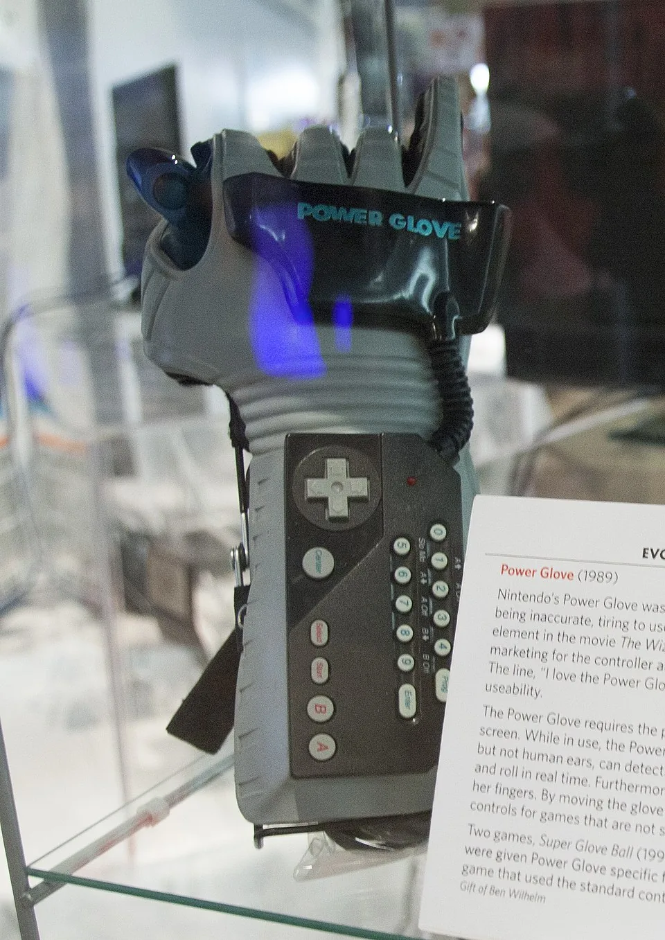A Nintendo Power Glove displayed upright inside a museum case