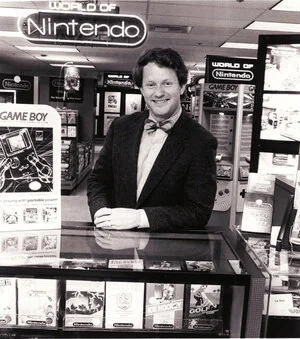 Howard Phillips wearing a bow tie behind a World of Nintendo retail display