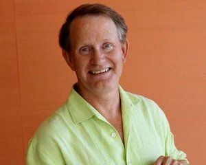 Later color portrait of Howard Phillips smiling in a green shirt