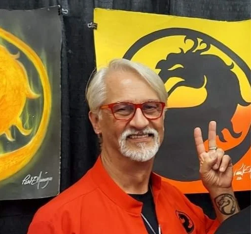 Paul Niemeyer wearing red glasses and an orange shirt in front of a Mortal Kombat dragon emblem